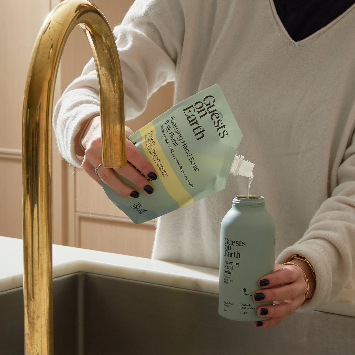 Guests on Earth Bulk Refill pouch pours foaming hand soap concentrate into a reusable bottle at the kitchen sink