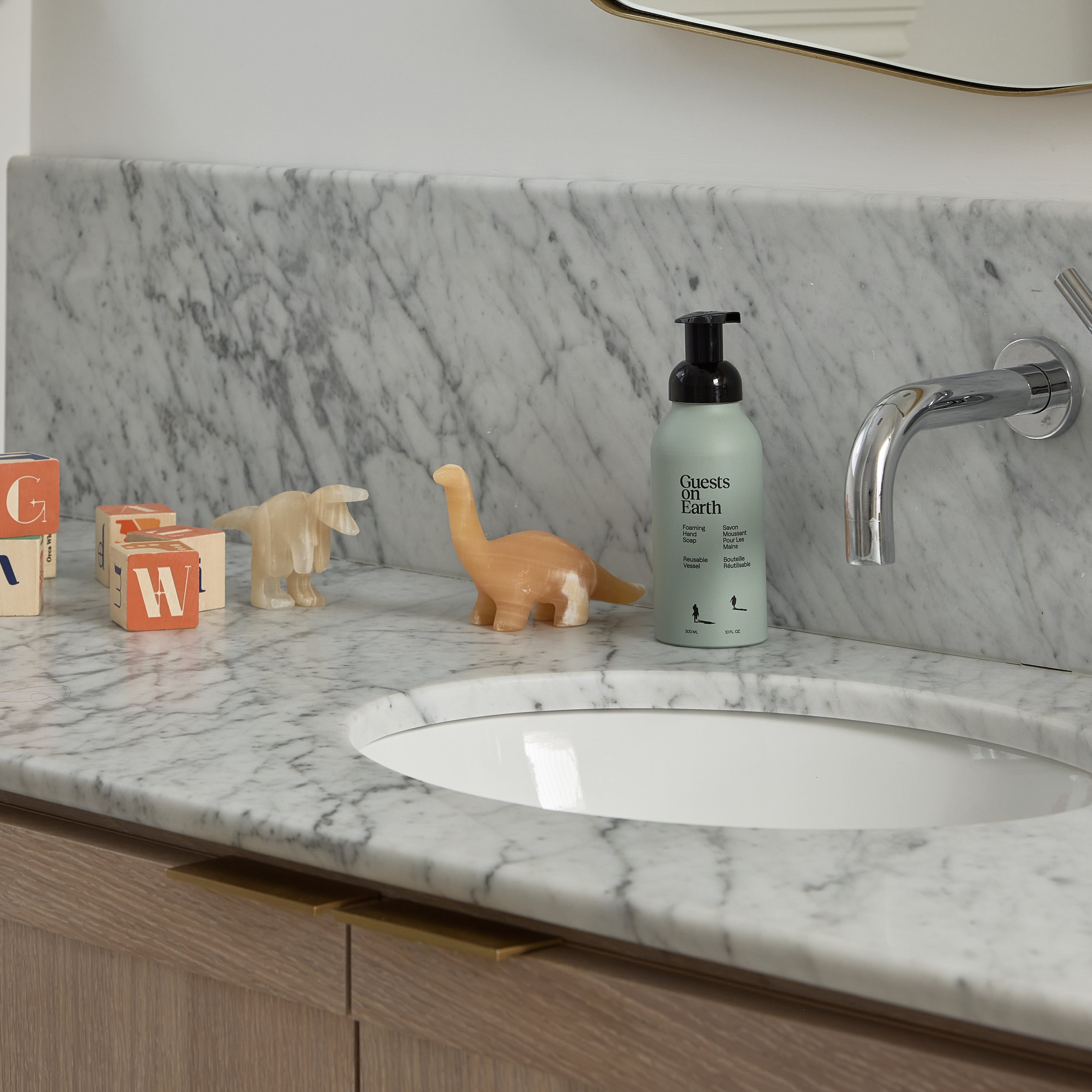 Guests on Earth Foaming Hand Soup on a marble vanity beside kids’ toys, styled by a chrome faucet and sink