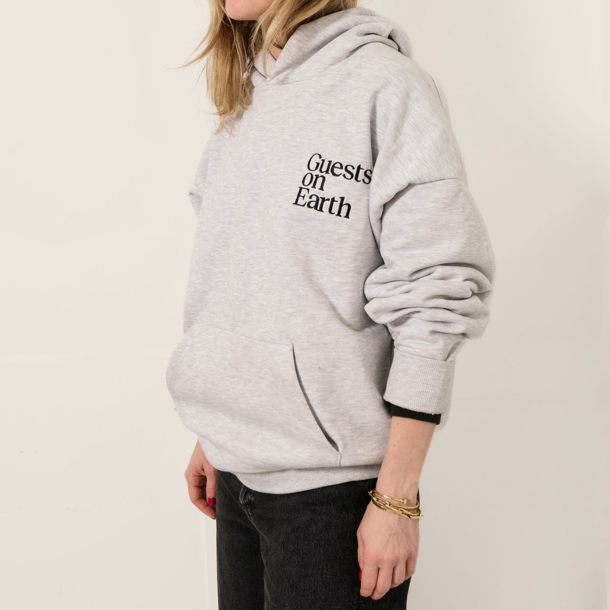 Woman wearing Guests on Earth Hoodie in heather grey, relaxed fit with bold chest logo and front pocket