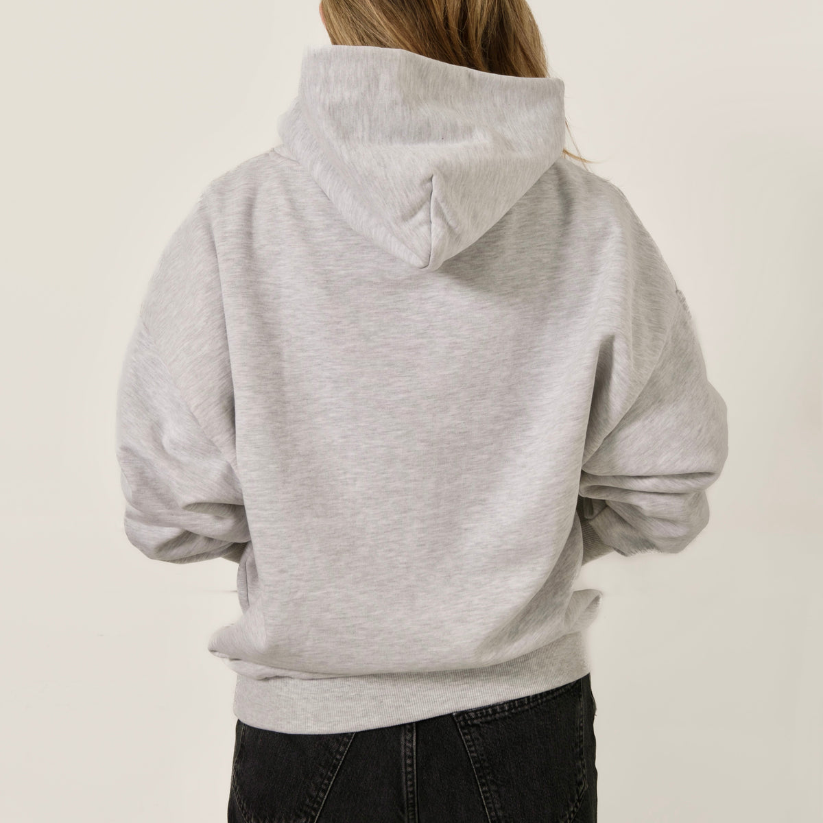 Woman wearing Guests on Earth Hoodie, back view in heather grey with hood up, clean unbranded back