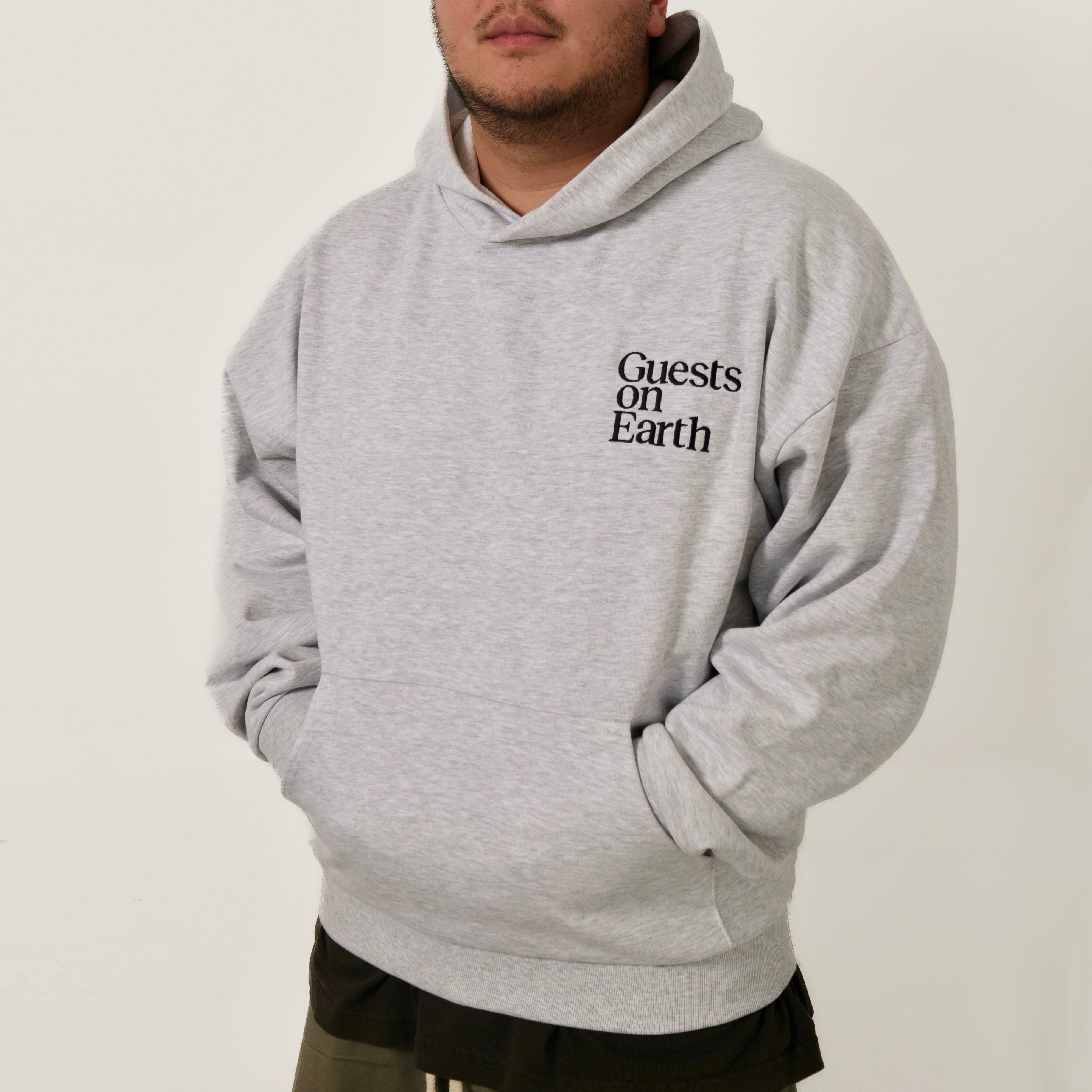 Guests on Earth Hoodie in heather grey, worn relaxed fit with minimalist chest logo and front pocket