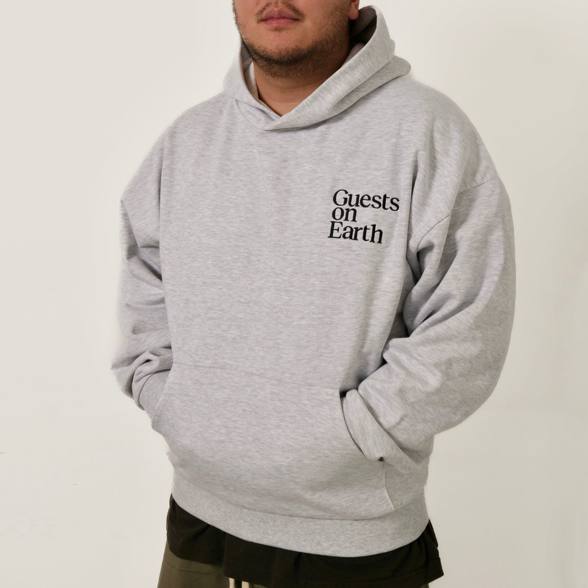 Guests on Earth Hoodie in heather grey, worn relaxed fit with minimalist chest logo and front pocket