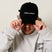 Guests on Earth black ambassador cap with white logo, worn by model adjusting the brim.