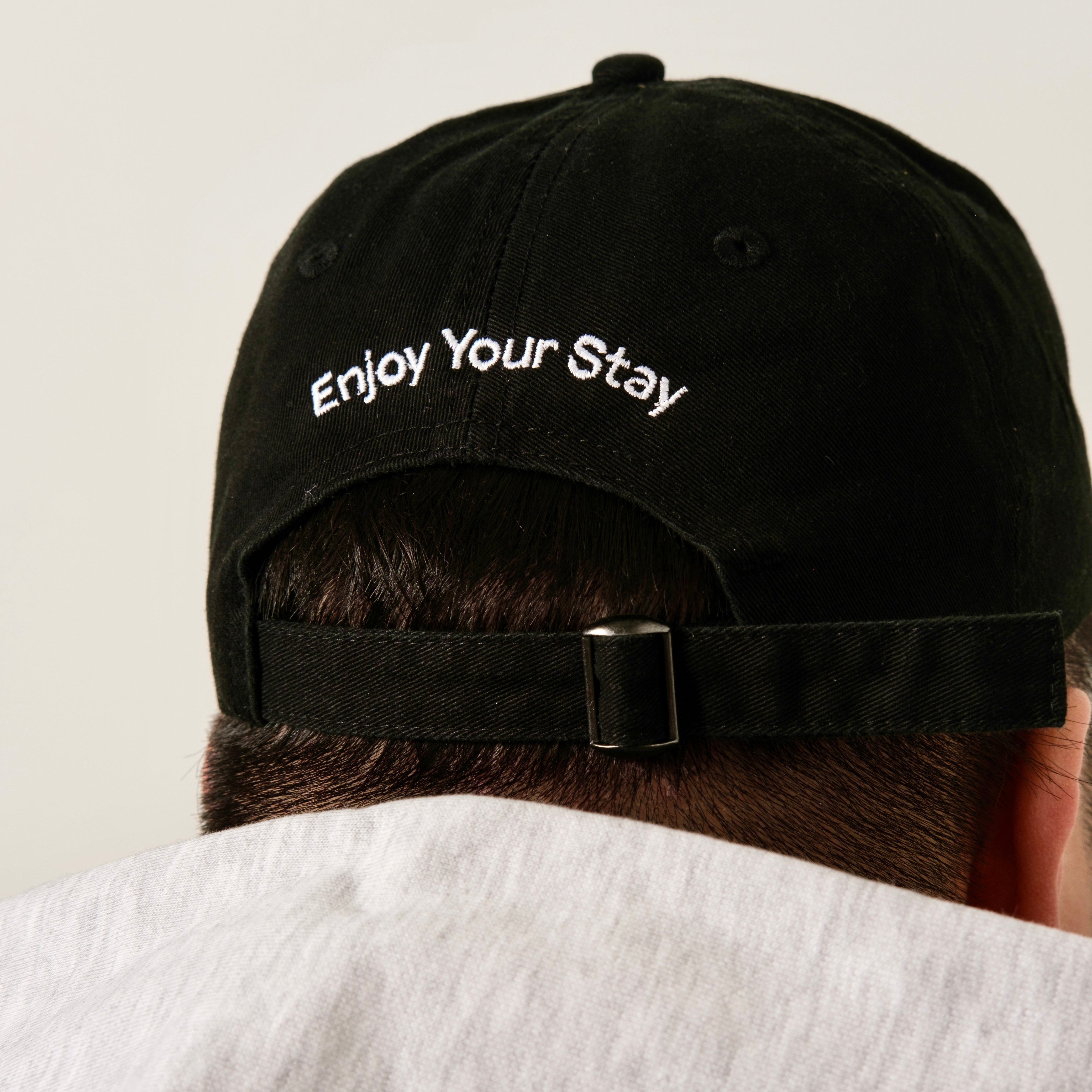 Guests on Earth black ambassador cap back view with Enjoy Your Stay embroidery and adjustable strap