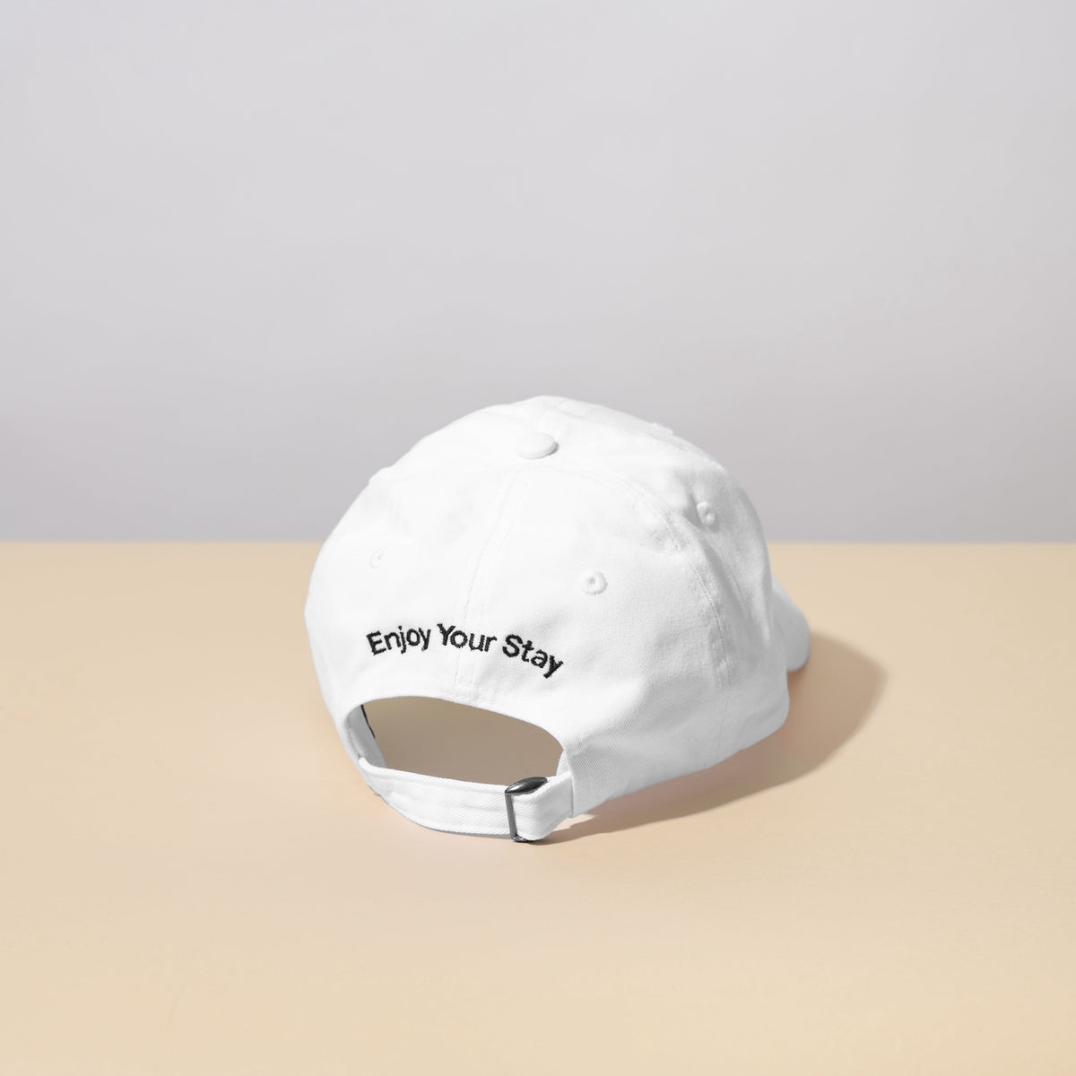 Guests on Earth Ambassador Cap back view: white adjustable strap with Enjoy Your Stay embroidery