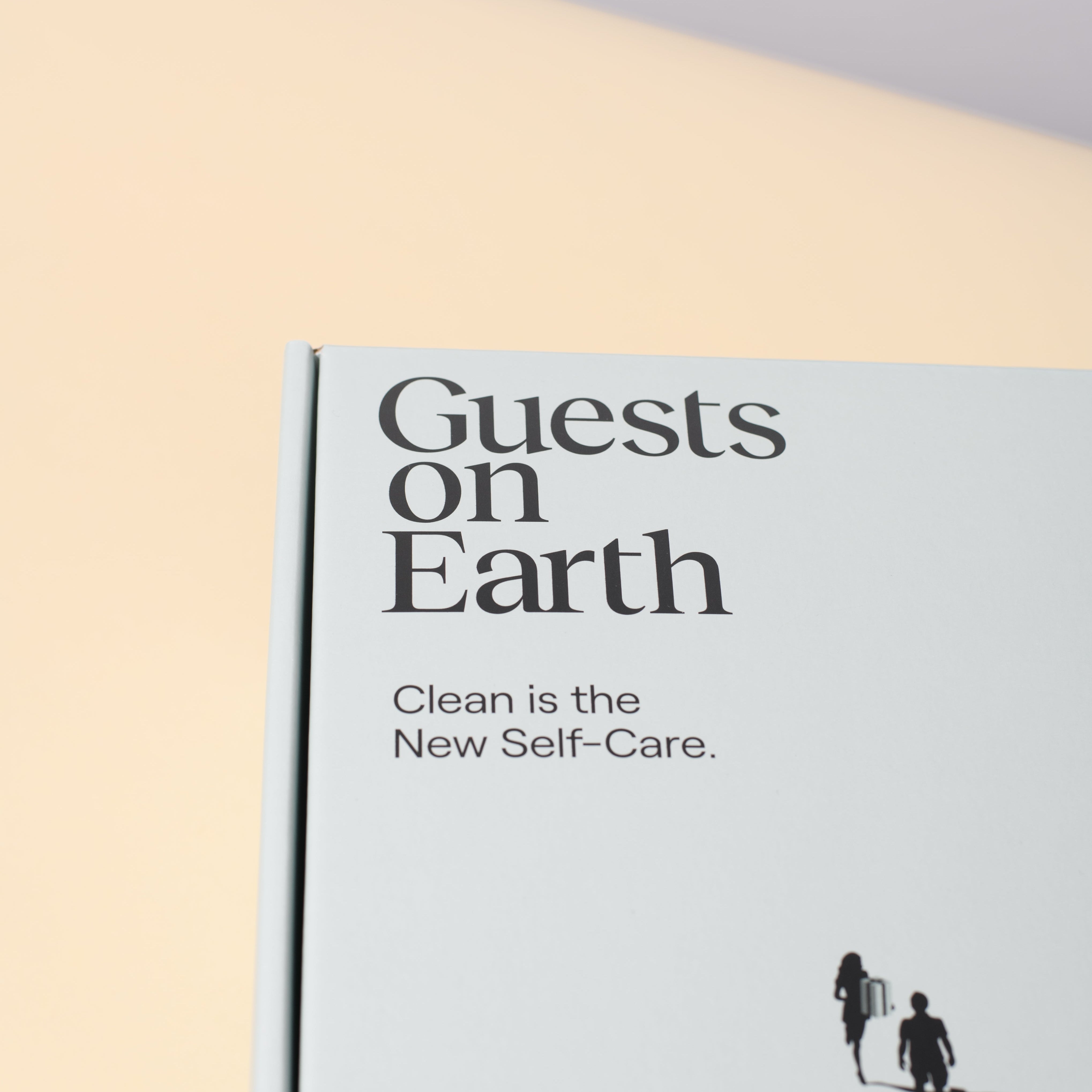 Guests on Earth gift box with minimalist white design and Clean is the New Self-Care text, close-up