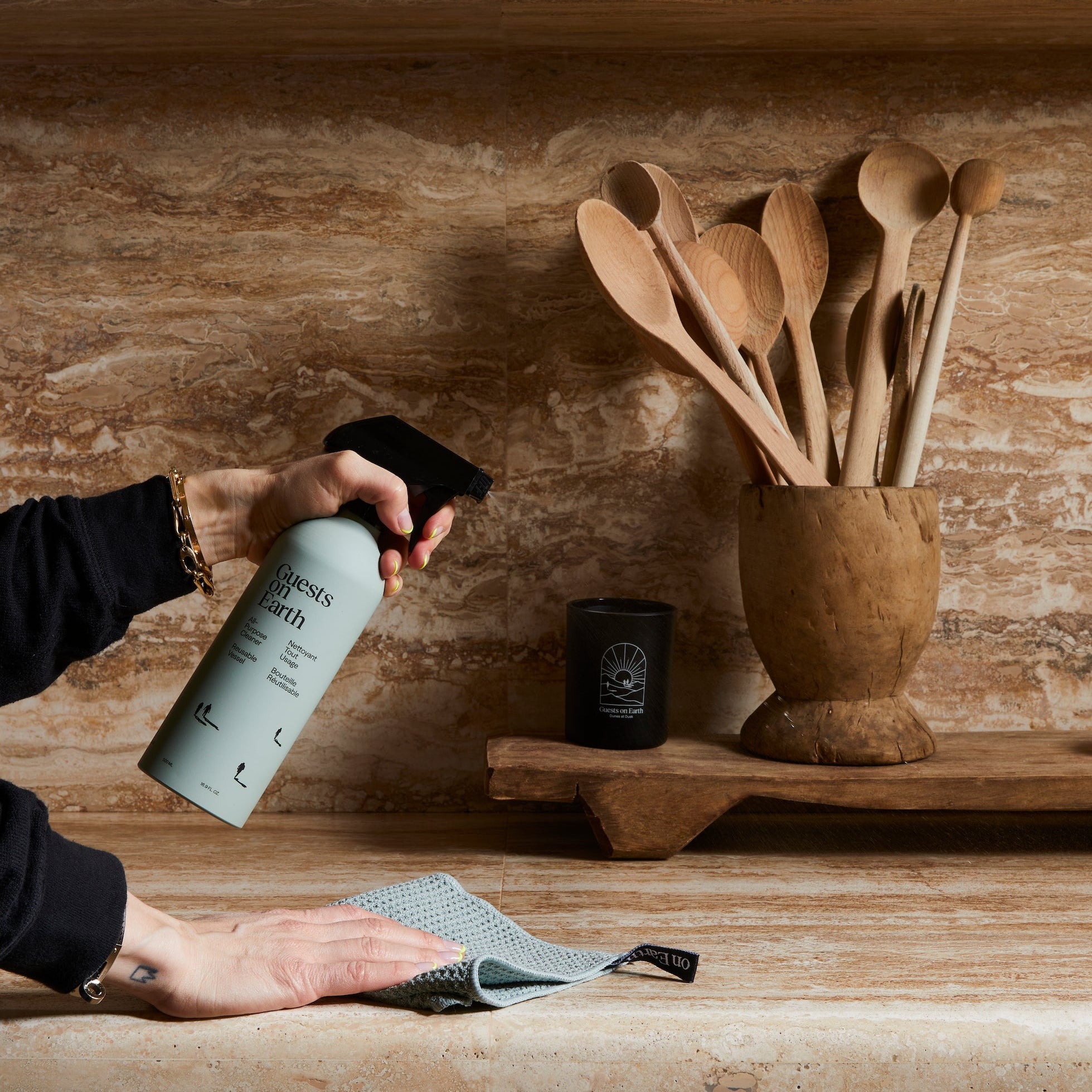 Guests on Earth All-Purpose Cleaner sprayed on kitchen counter as cloth wipes near wooden utensils