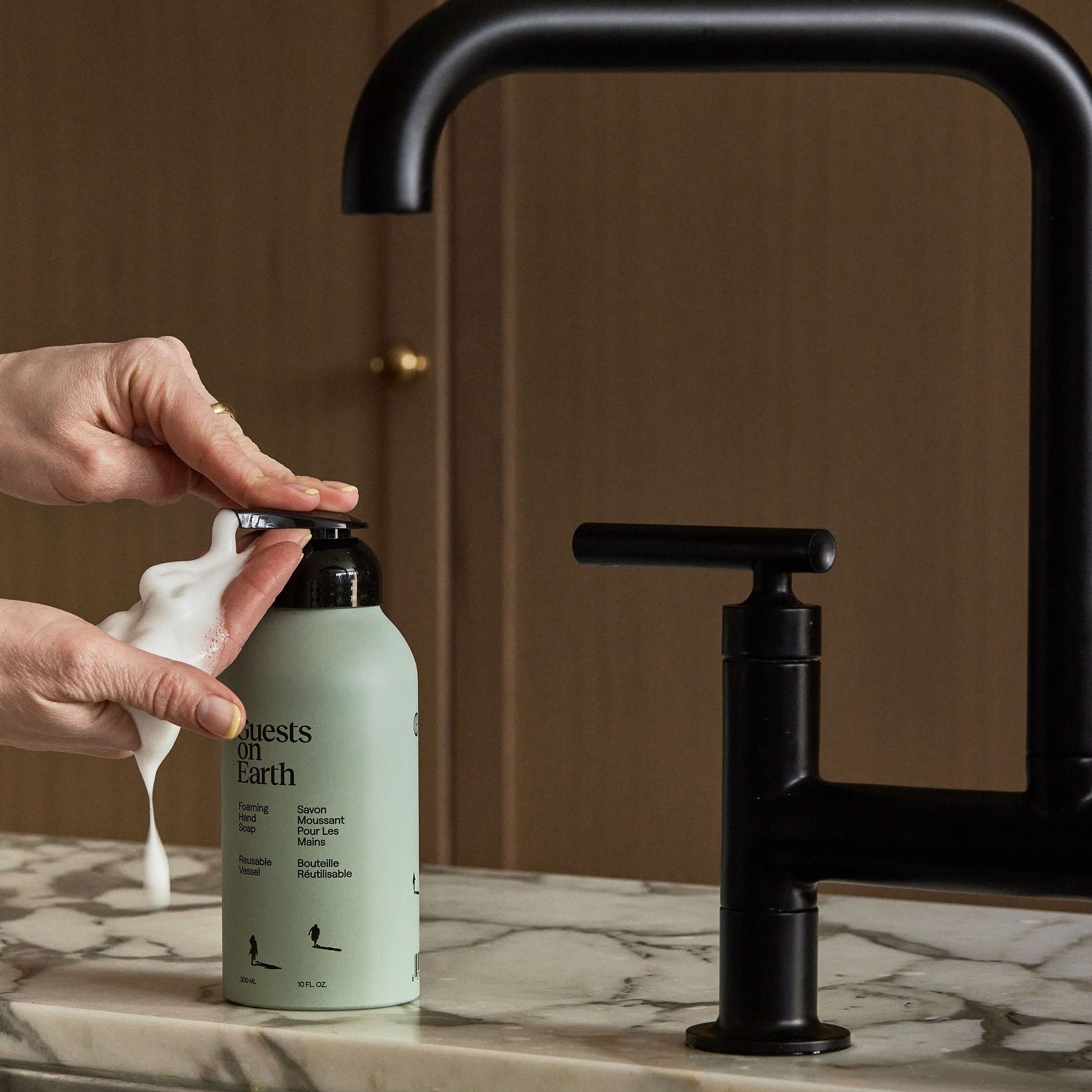 Guests on Earth Foaming Hand Soap dispensed in creamy foam beside matte black faucet on marble countertop