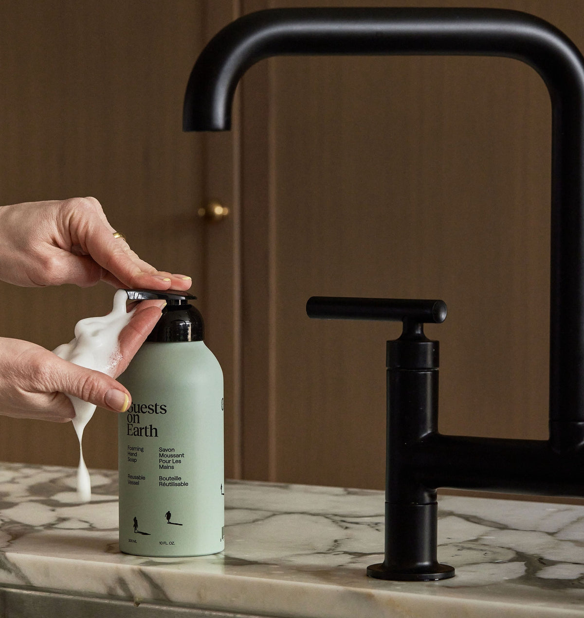 Guests on Earth Foaming Hand Soap dispensed in creamy foam beside matte black faucet on marble countertop